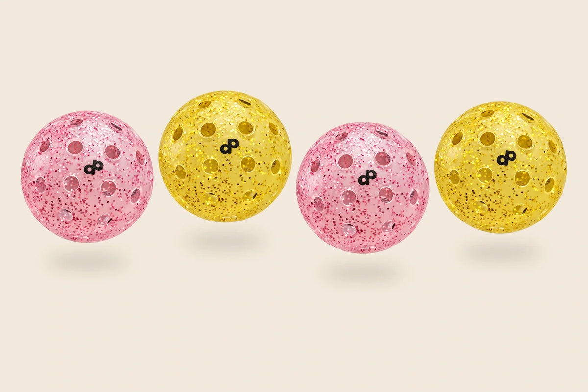 Two pink and two yellow glitter pickleballs with a visible DP logo on every ball, arranged above soft shadows on an off-cream background.