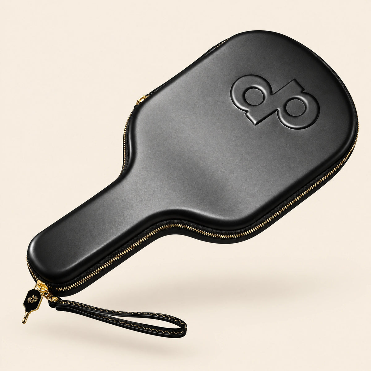Full three-quarter view of the black High Roller paddle case with embossed DP logo, gold zipper and wrist loop, floating on cream.