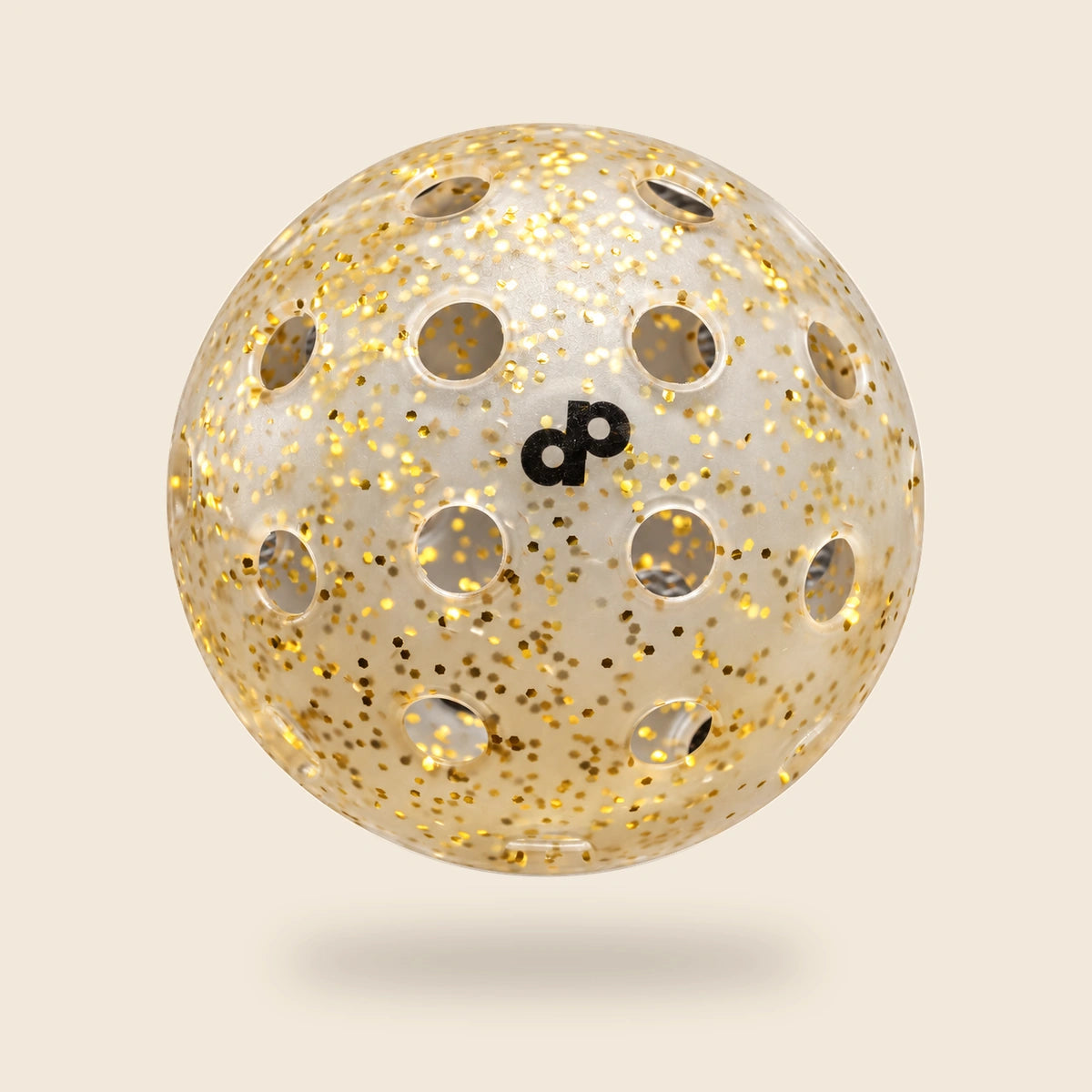 High Roller translucent gold glitter pickleball with black DP logo and offset round-hole rows, floating on an off-cream background.
