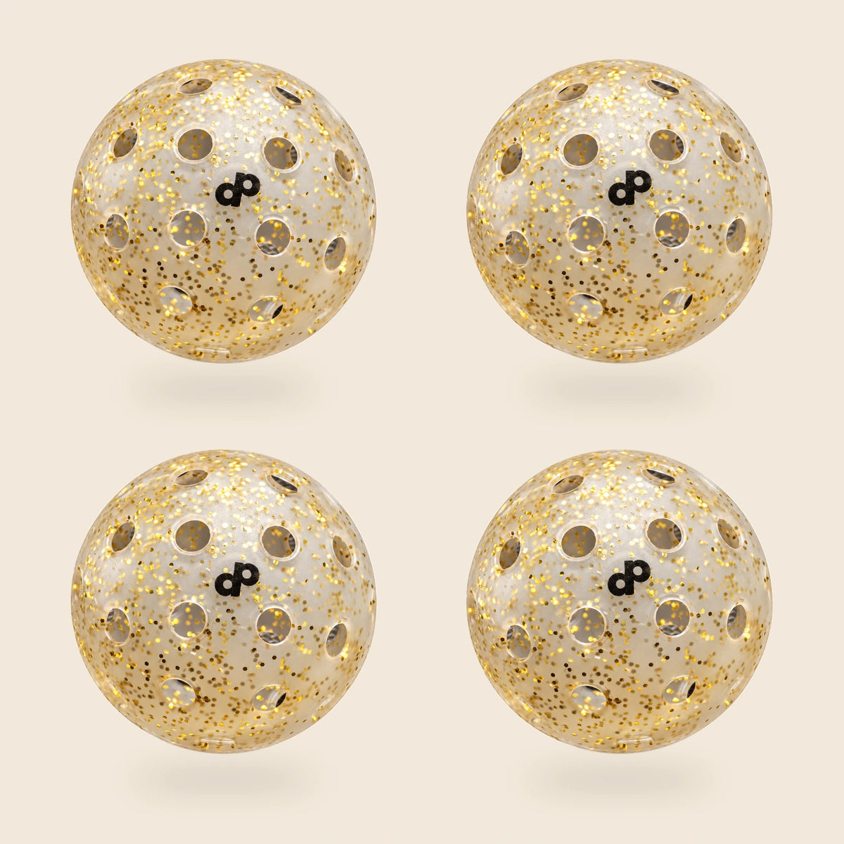 4 gold glitter pickleballs, each with a visible black DP logo and offset hole rows, floating above soft shadows on an off-cream background.