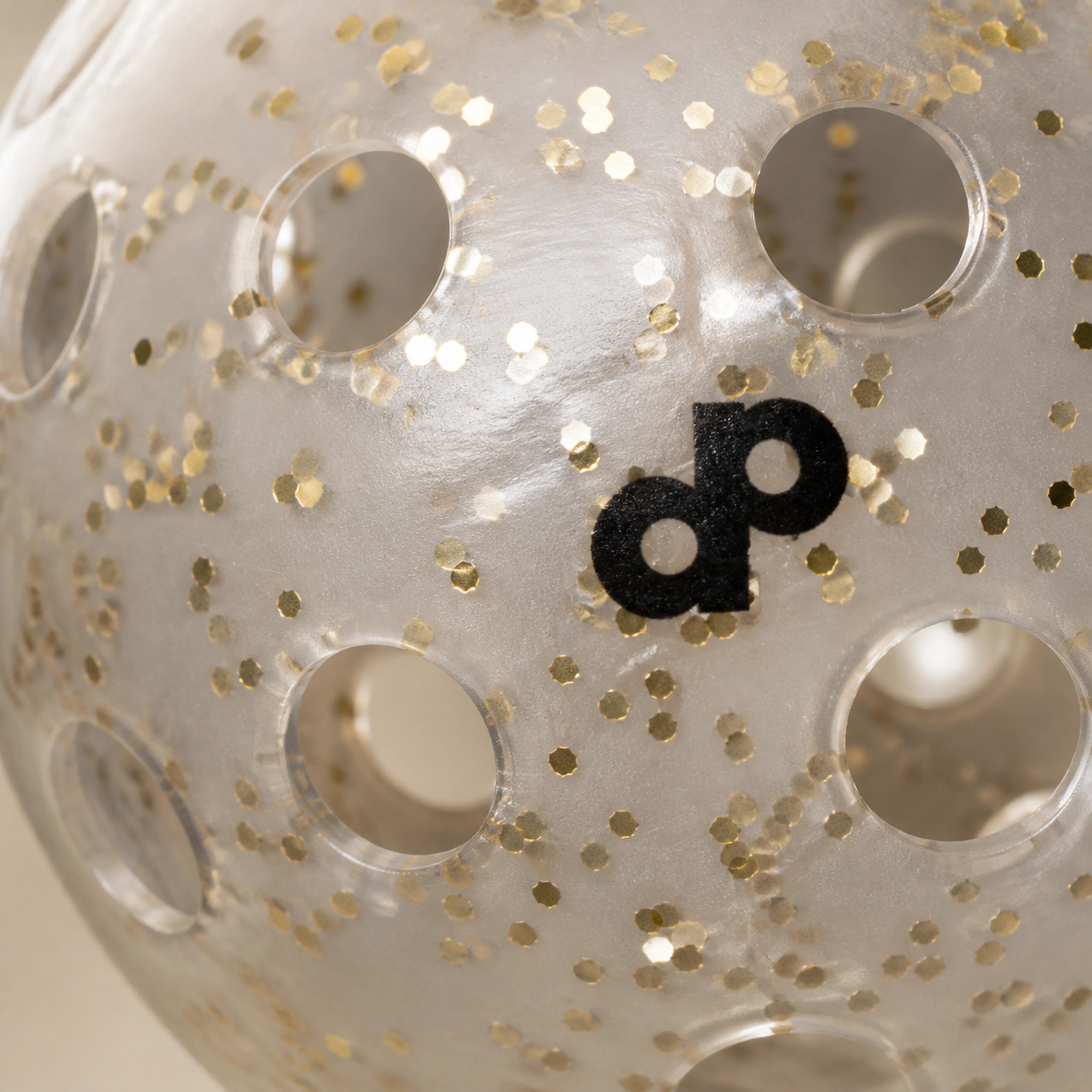 Macro view of metallic gold glitter, molded hole rims, and clear shell on a DOPE pickleball
