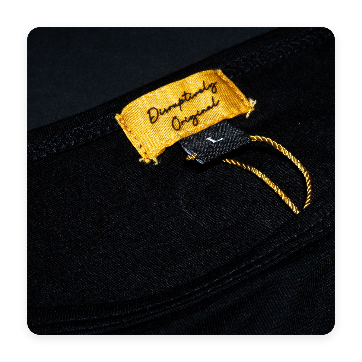 Real photograph of the gold Disruptively Original neck label and black knit fabric, presented on the brand cream.