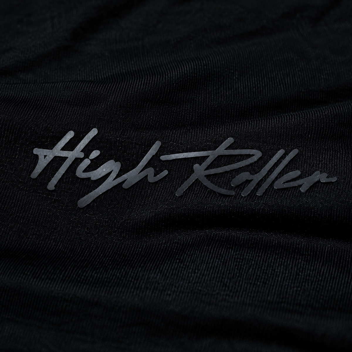 Close-up of the complete tonal charcoal High Roller rubber script on fine black bamboo-cotton jersey.