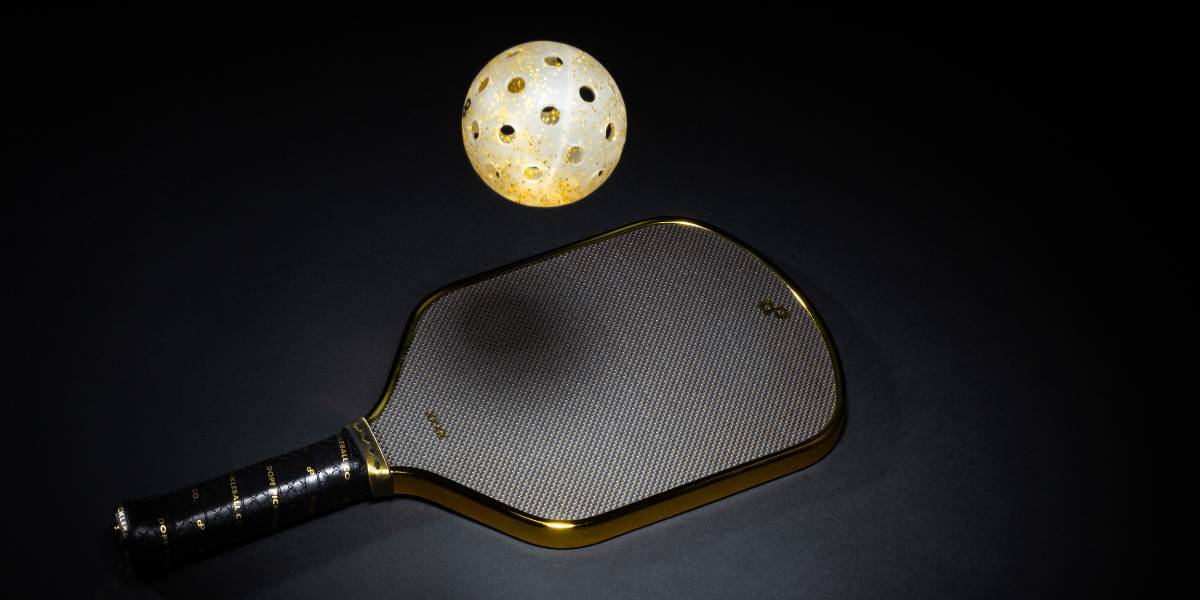 A Dope Pickleball Co Gold Glitter-Infused Pickleball Ball bouncing on The High Roller Paddle.