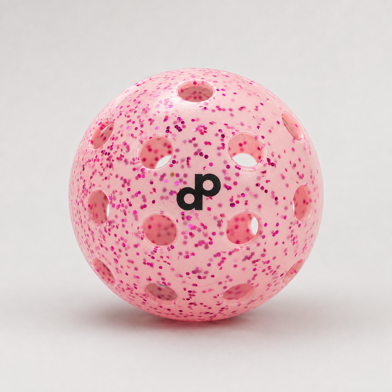 Pink glitter-infused outdoor pickleball on a clean studio background
