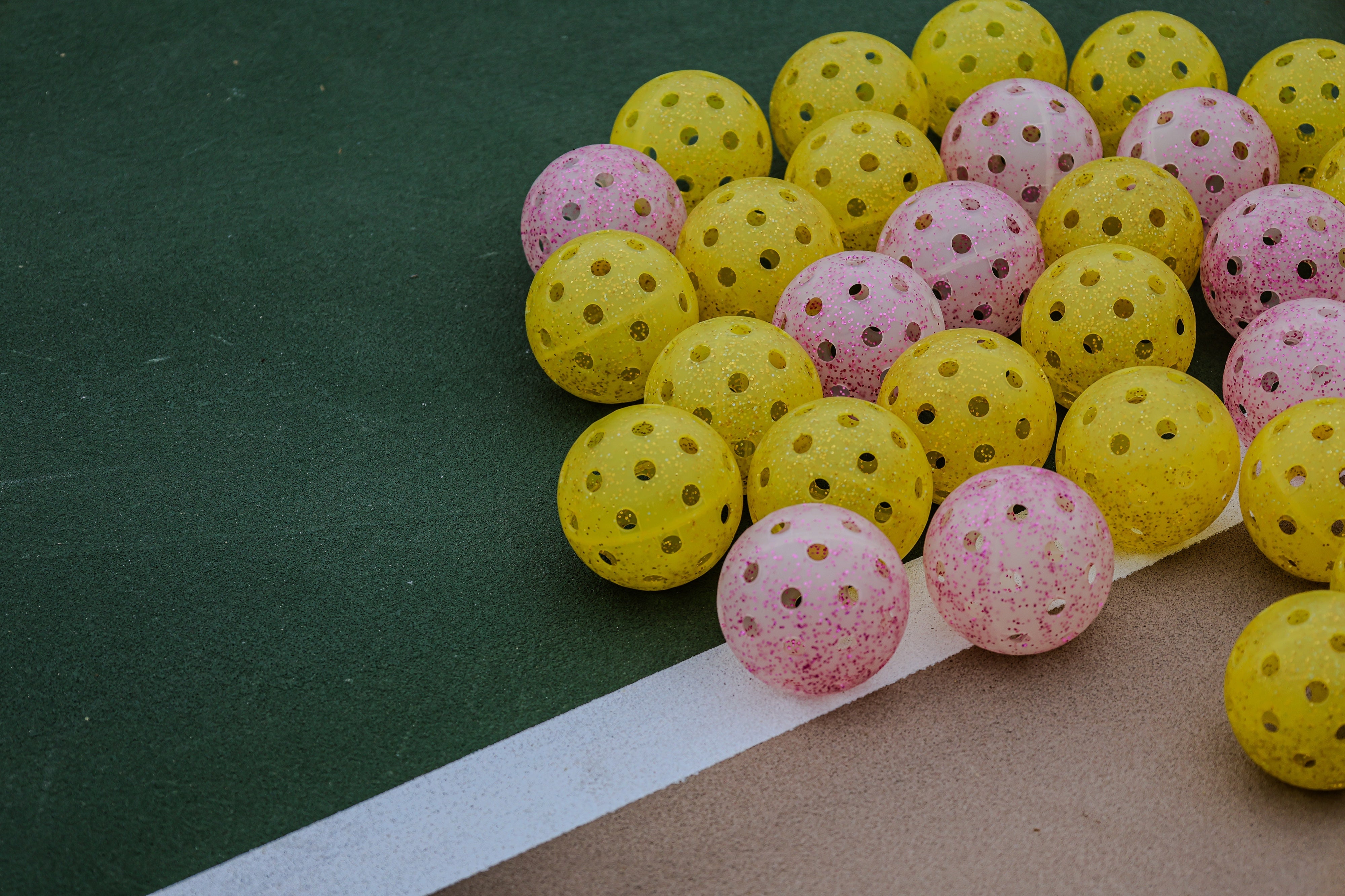 Real DOPE pink and yellow glitter pickleballs photographed together on a green outdoor court