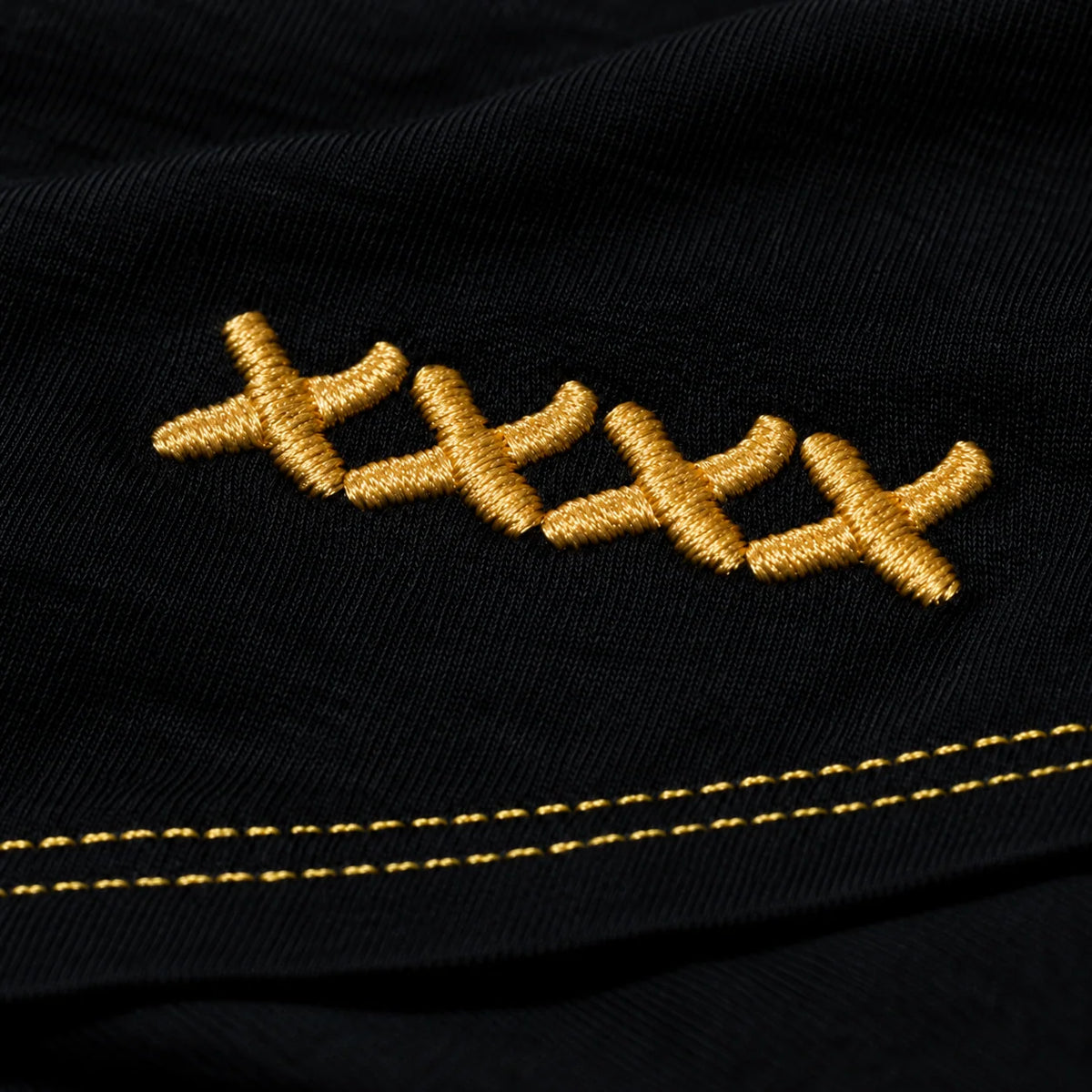 The actual High Roller shirt hem with four linked gold embroidered Xs and two parallel rows of gold stitching.