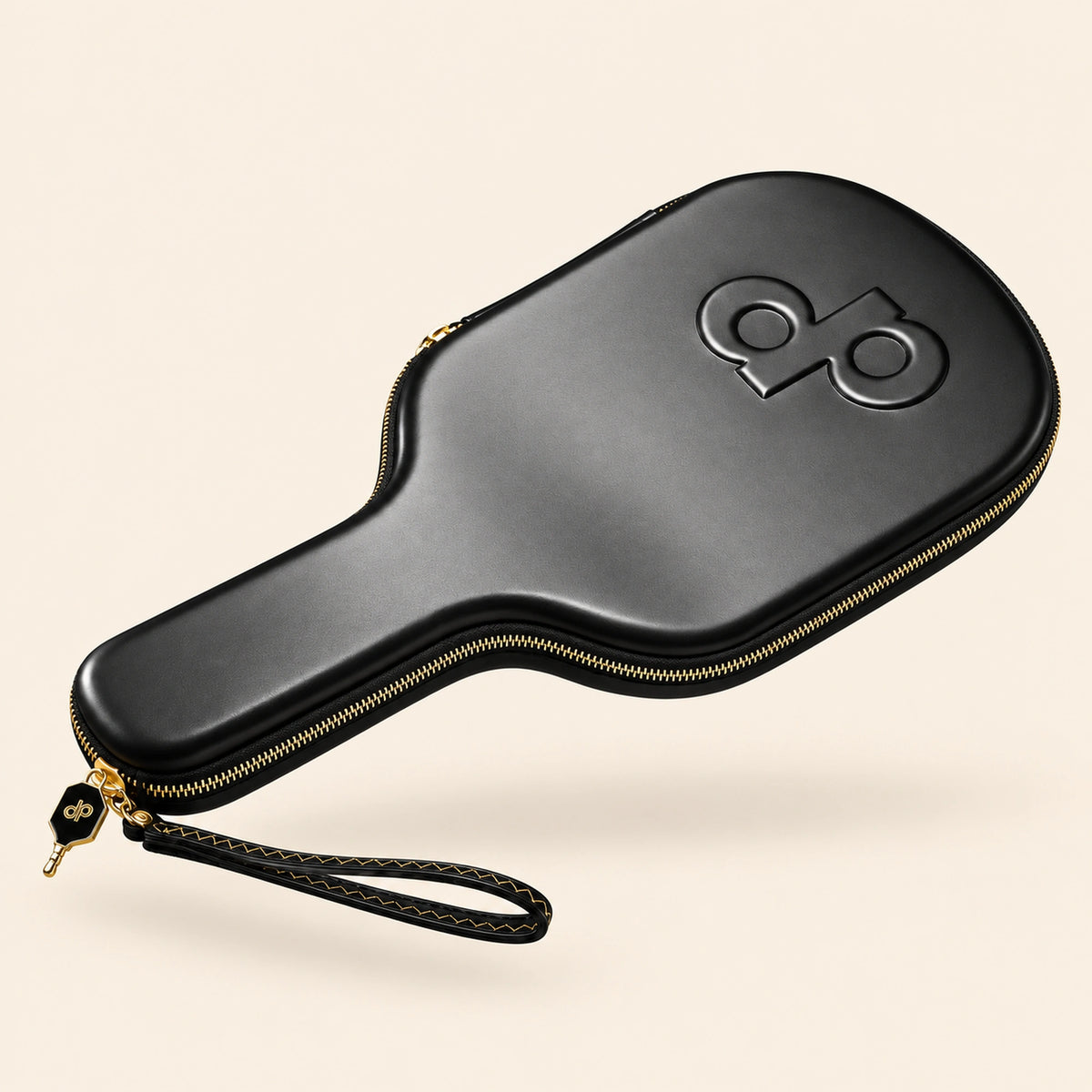 Full oblique front view of the black High Roller paddle case with embossed DP logo, gold zipper and wrist loop, floating on cream.