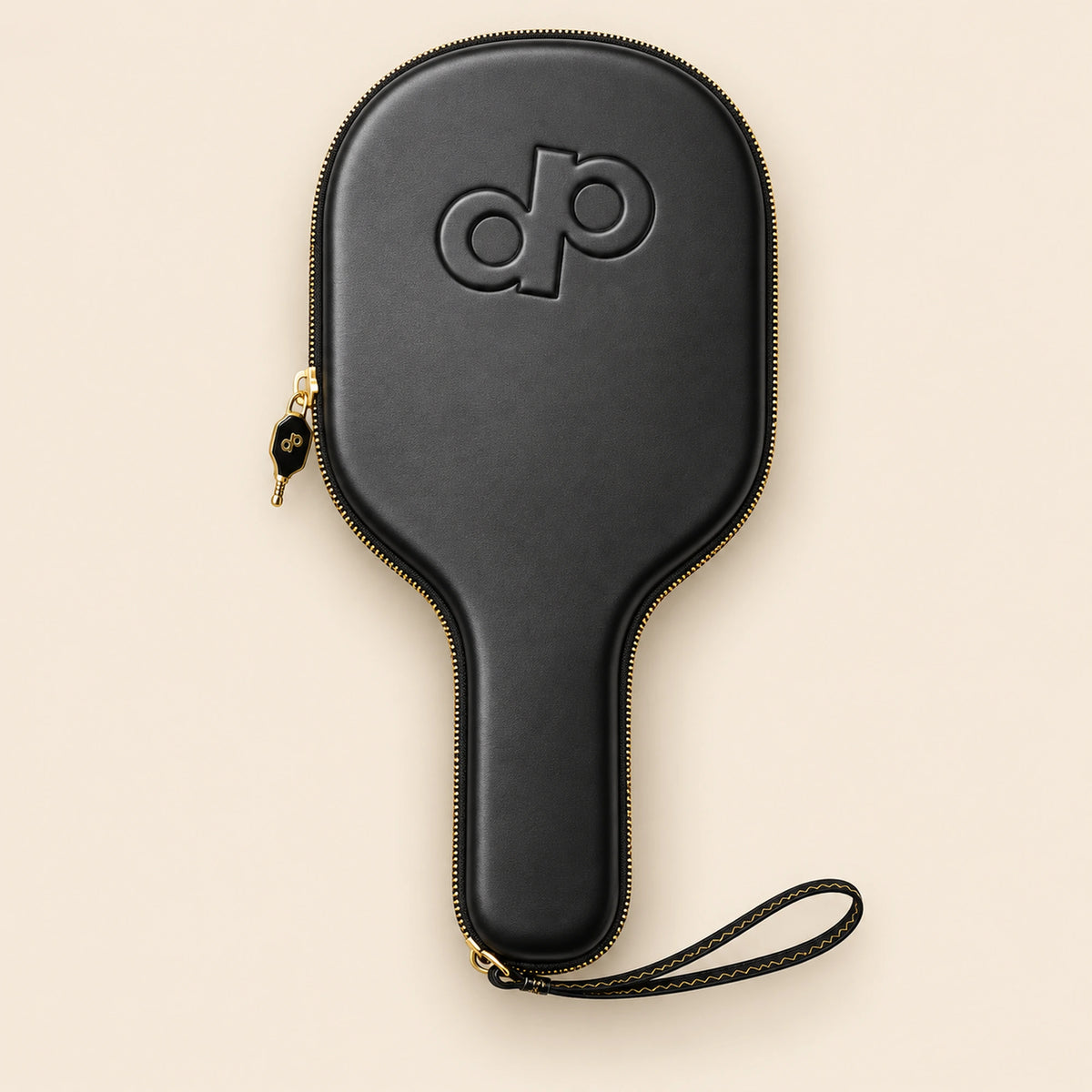 Full overhead view of the black High Roller paddle case with embossed DP logo, gold zipper and stitched wrist loop, floating on cream.