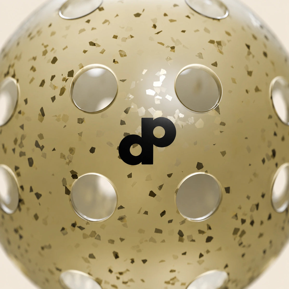 Close-up of the High Roller pickleball's pale champagne shell, gold glitter, black dp logo and surrounding holes on cream.