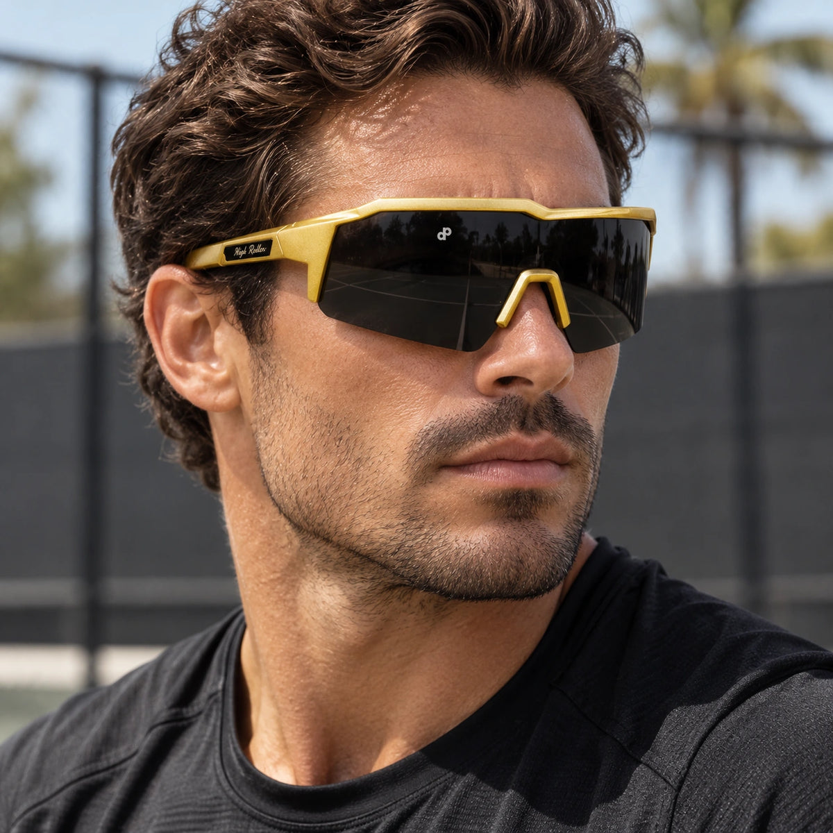 Gold High Roller shield sunglasses worn courtside, with dark continuous lens and signature temple detail.