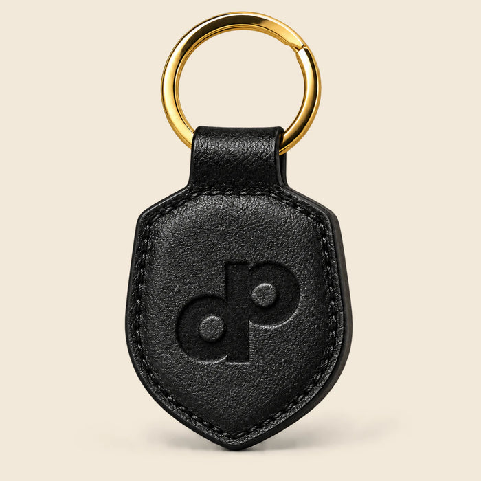 Black leather paddle-shaped keychain with debossed DP monogram, finished edges and a gold-tone split ring.