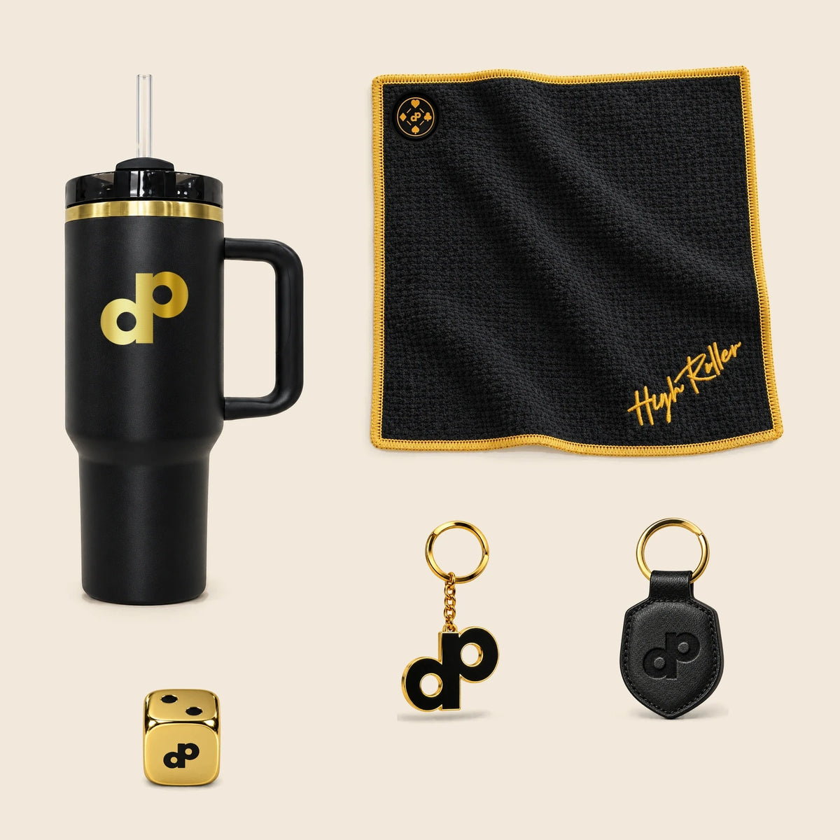 High Roller tumbler, magnetic towel, gold logo keychain, leather keychain and one gold metal die arranged on cream.