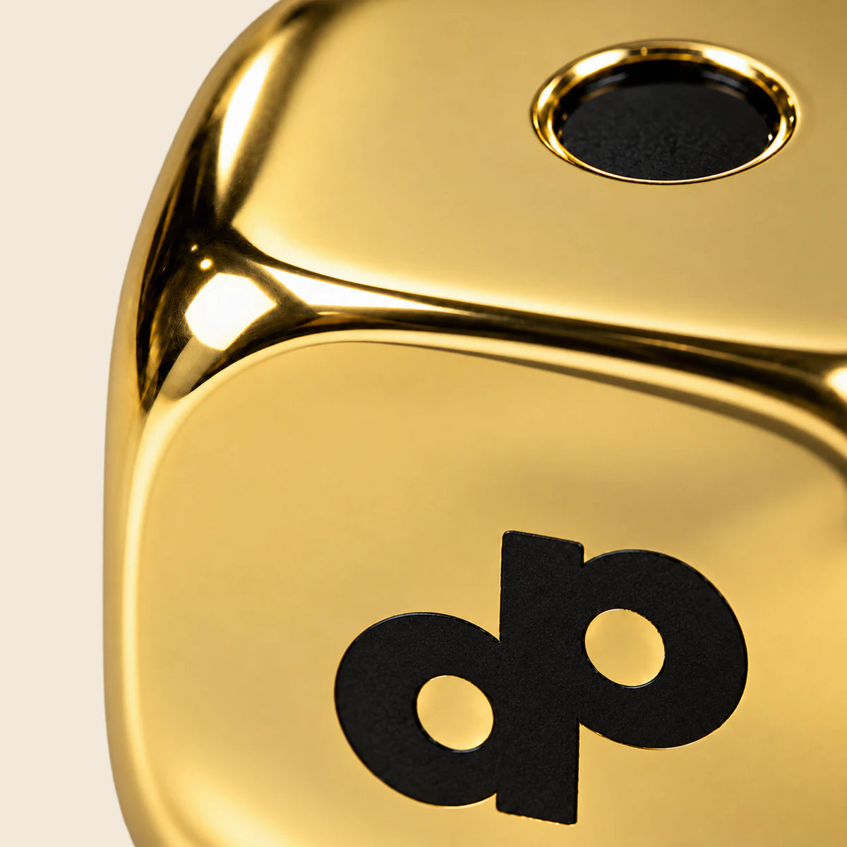 Close-up of a smooth polished gold High Roller die, its black DP logo and recessed pip.
