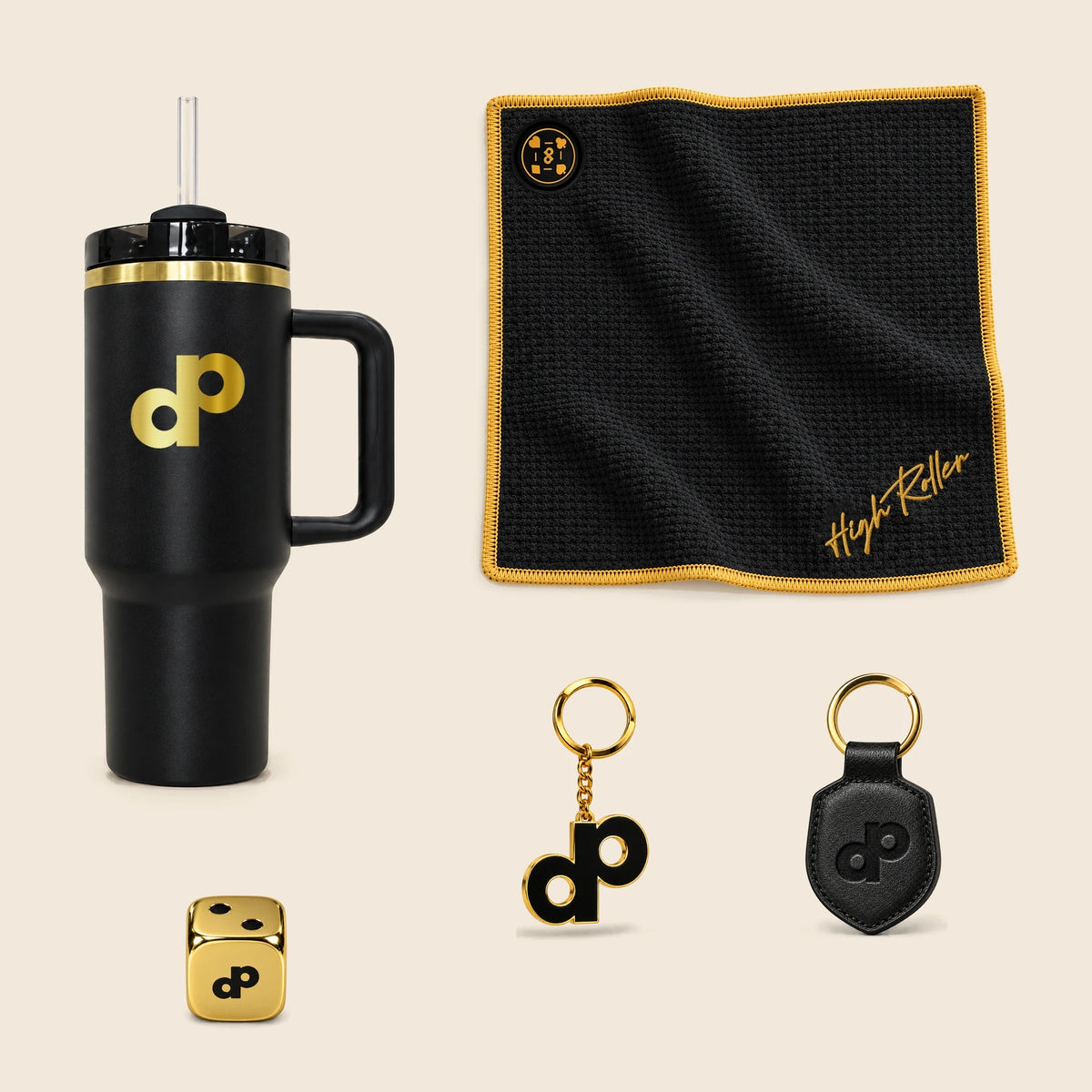 Full-height High Roller tumbler, magnetic towel, gold logo keychain, leather keychain and one gold metal die from the bundle, arranged on cream.