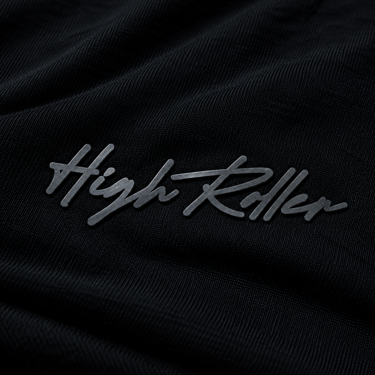 Macro photograph of the complete subtle charcoal-gray High Roller rubber script on fine black bamboo-cotton jersey.