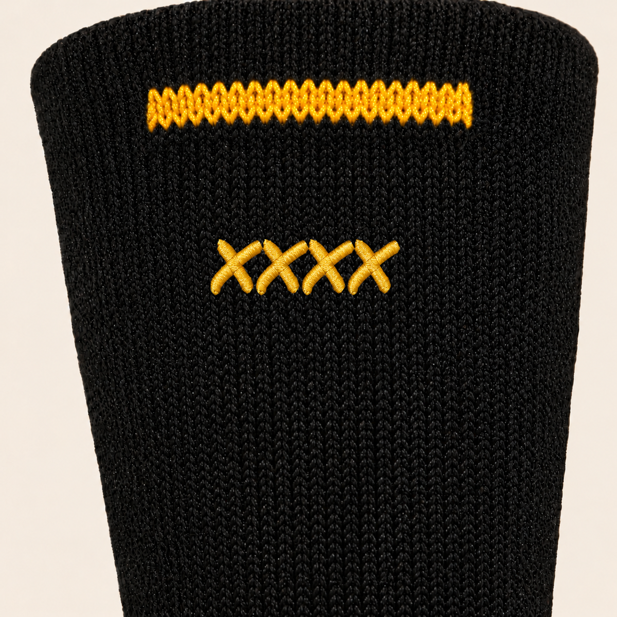 High Roller rear sock cuff close-up on theme cream, showing four gold satin embroidered Xs in the actual Permanent Marker font, fine black knit and a neat gold rear cuff stripe ending before both sides.
