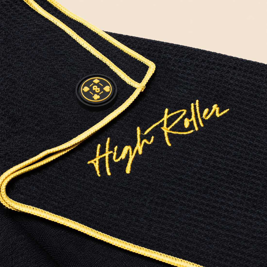 High Roller towel in its photographed folded arrangement, with gold stitching and the sewn magnet inset from the corner.