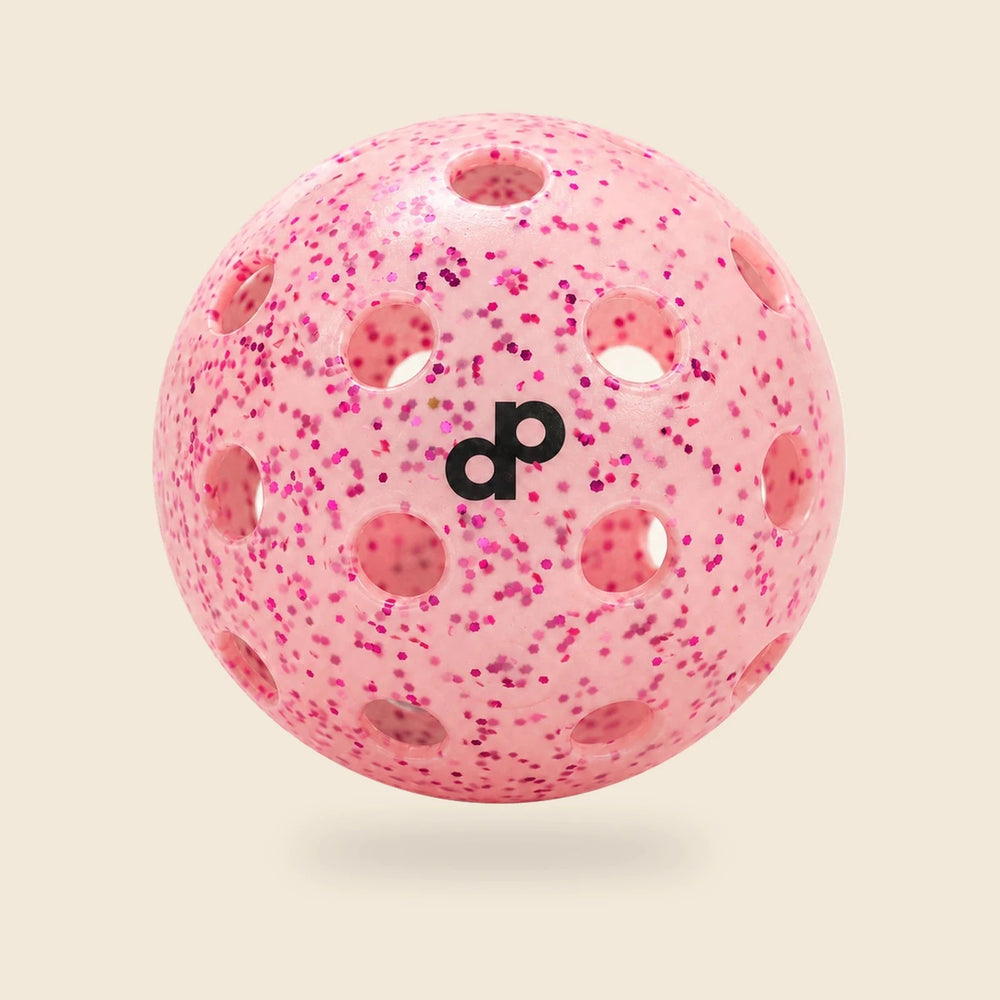 Single pink Dope glitter pickleball with black DP logo and circular holes on a cream background.