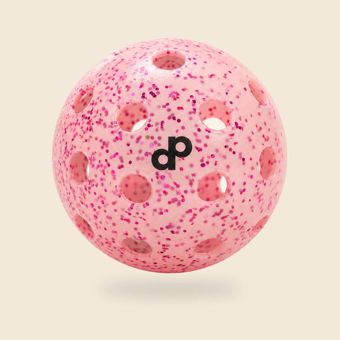 Single pink DOPE glitter pickleball with black DP logo and circular holes on a cream background.