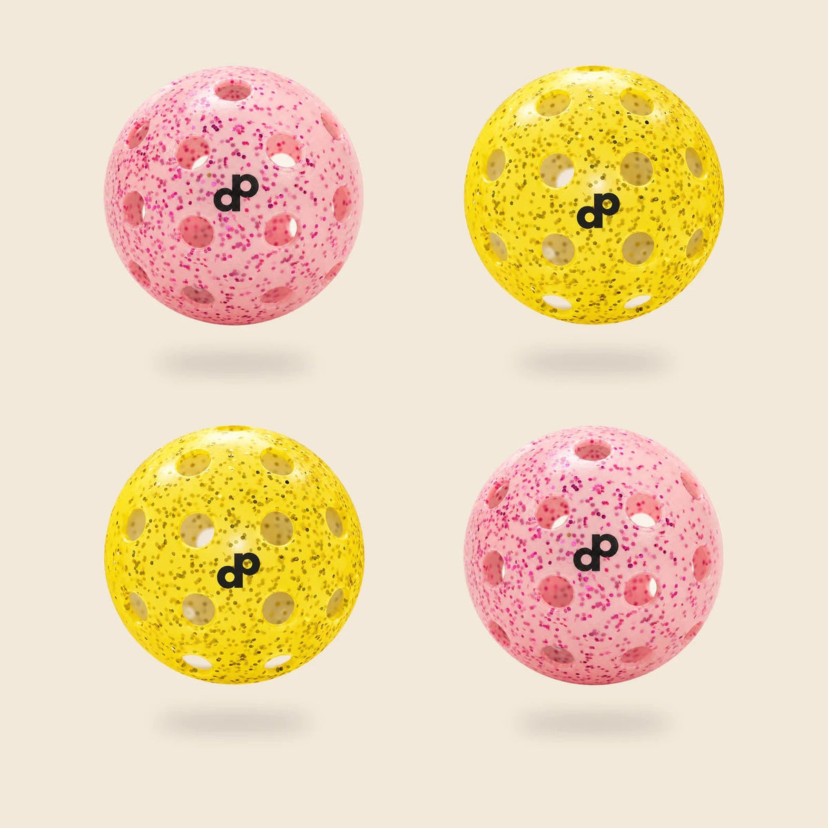 4 DOPE glitter pickleballs, half pink and half yellow, each with a black DP logo, floating on cream.