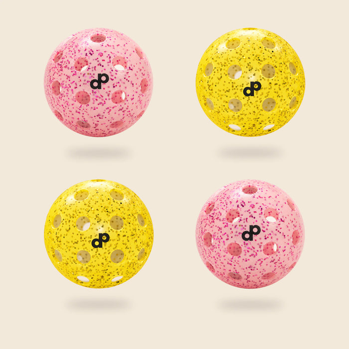 4 DOPE glitter pickleballs, half pink and half yellow, each with a black DP logo, floating on cream.