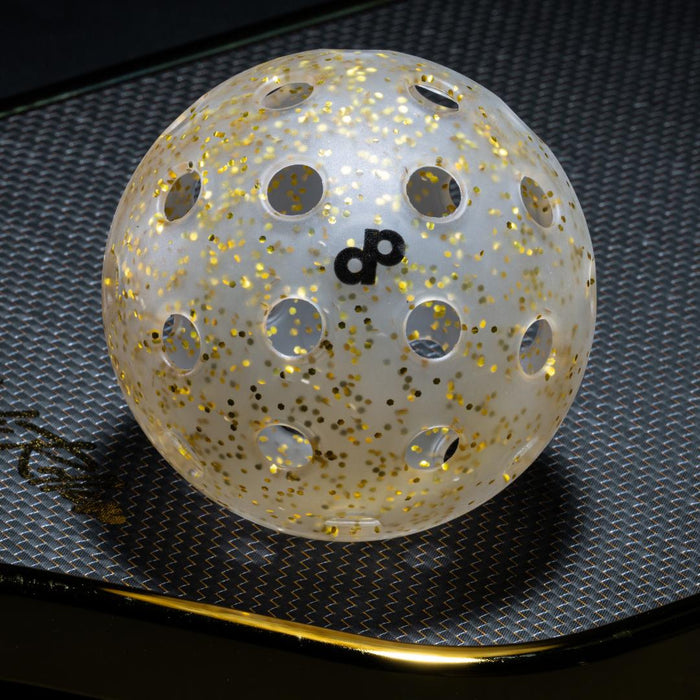 Real clear DOPE pickleball with gold glitter and black monogram photographed on a black High Roller paddle