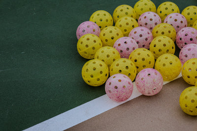 Real DOPE yellow and pink glitter pickleballs photographed together on a green outdoor court