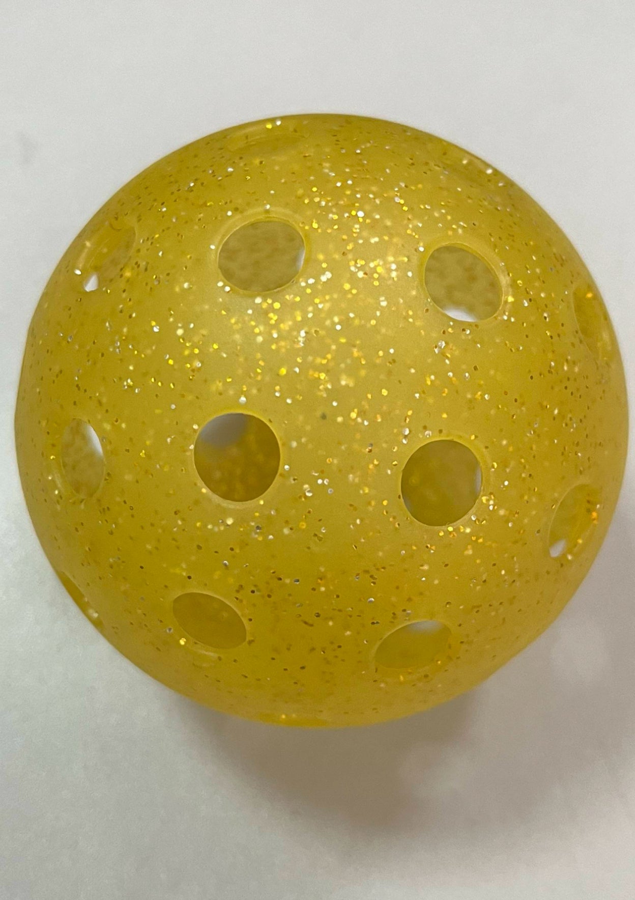 Real translucent yellow DOPE pickleball with uneven gold glitter, molded holes, and visible interior walls