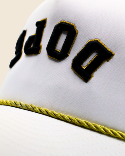 Close-up of black-and-gold DOPE embroidery and gold rope trim on a white hat