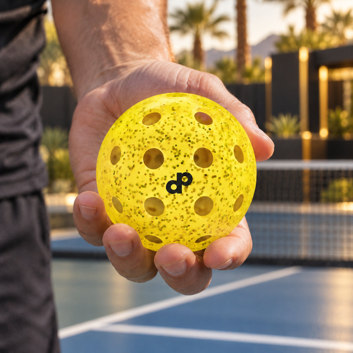 Yellow glitter pickleballs held beside a Las Vegas resort court in warm afternoon light.