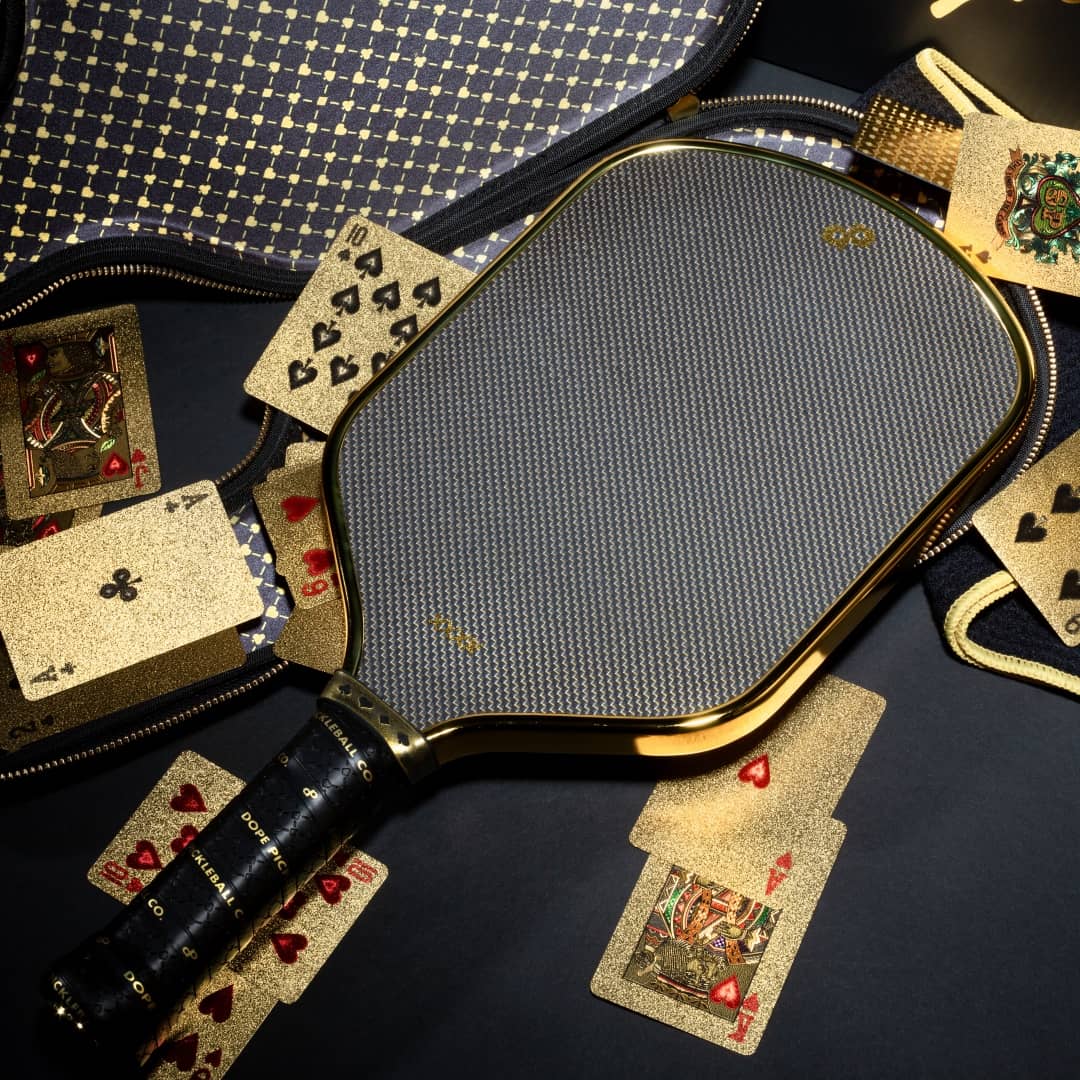 A showcase of the High Roller Gold Pickleball Paddle with the options Paddle Case, with some glittery gold playing cards scattered around.