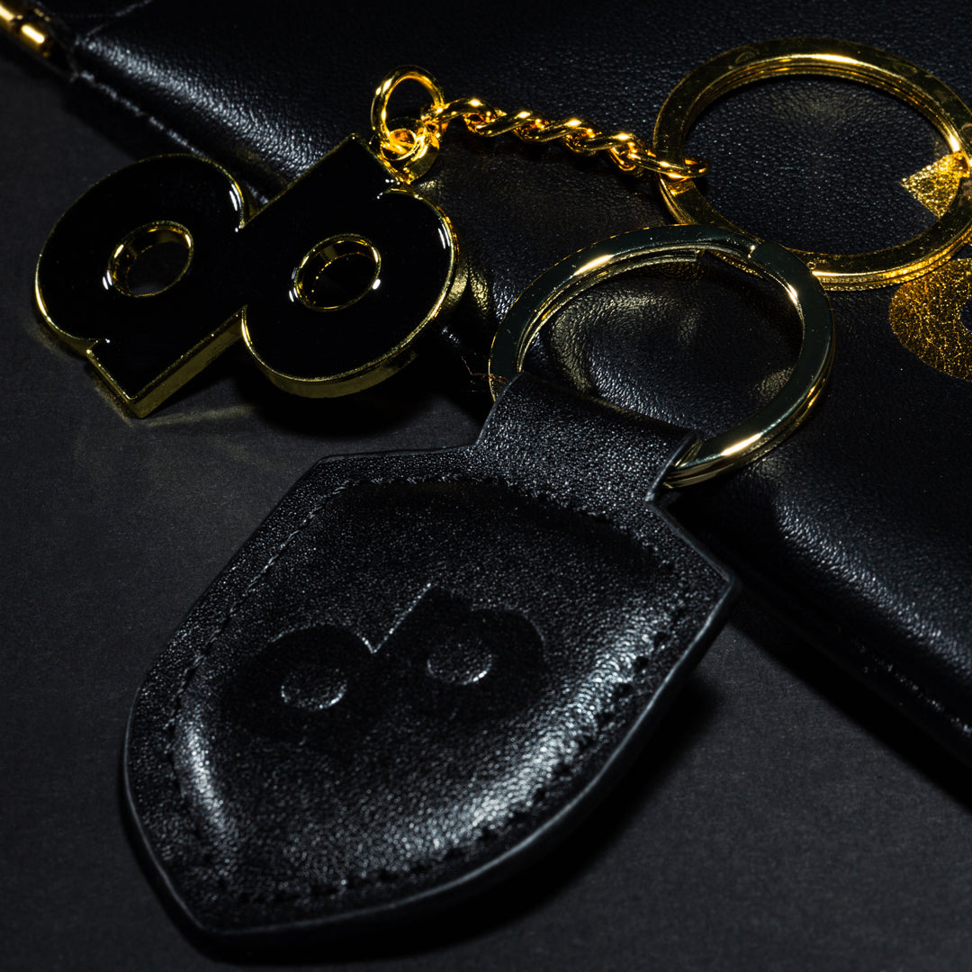 Black paddle-shaped tag, black-and-gold dp keychain, and metal key rings on a black surface