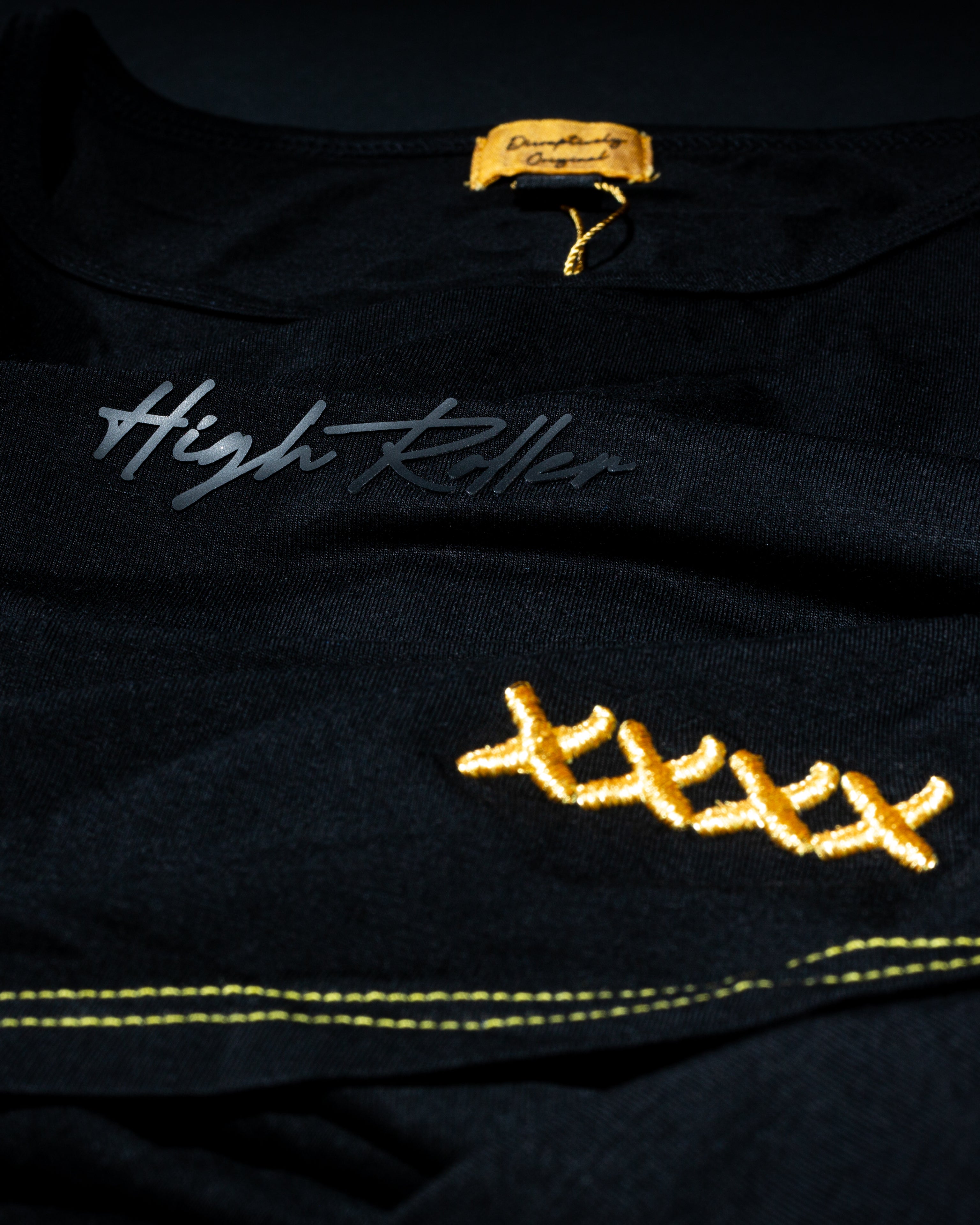 Close-up of High Roller script and gold stitch detail on a black T-shirt