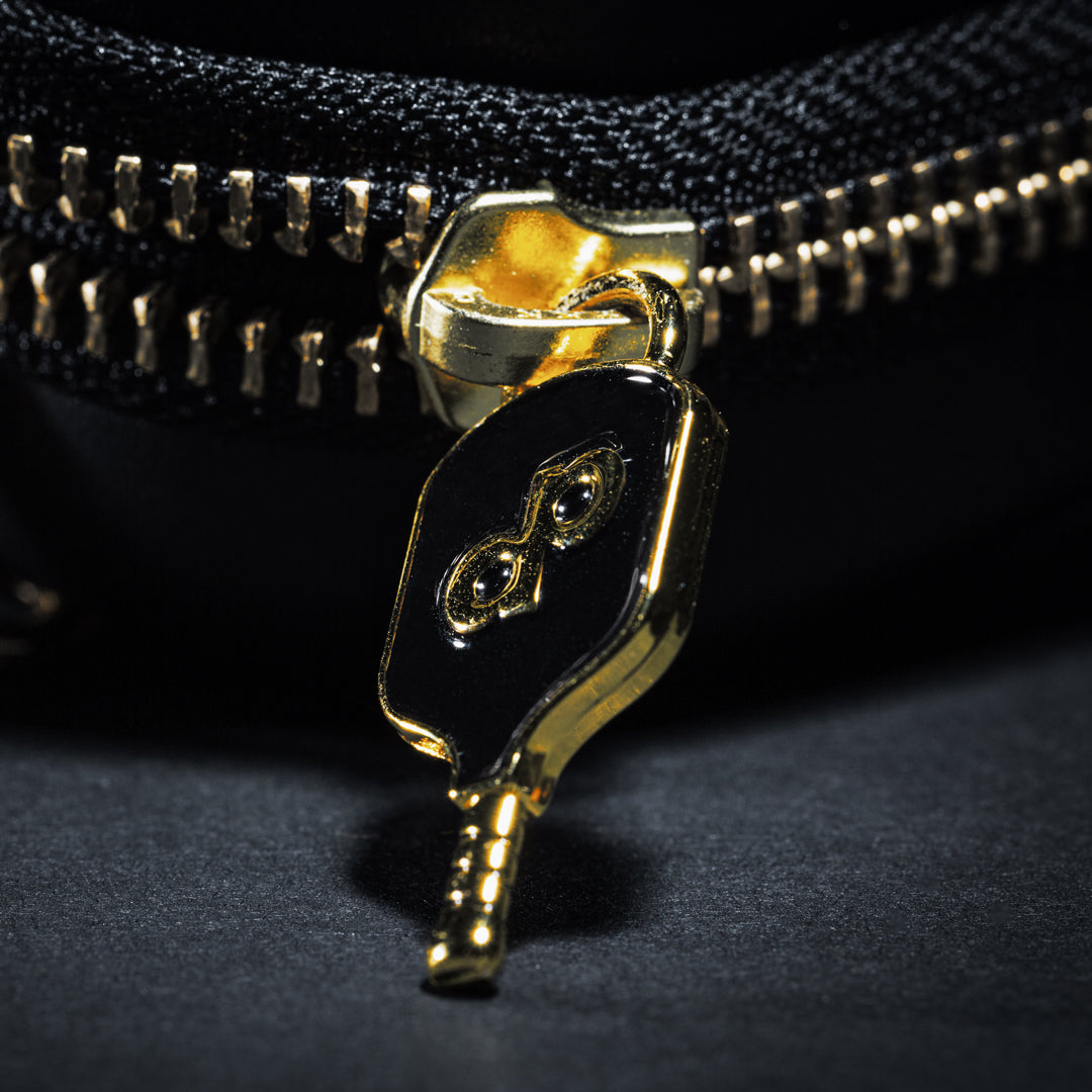 Close-up of a black-and-gold dp-logo zipper pull on the High Roller paddle case