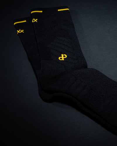 Pair of black High Roller socks with gold dp and stitch details on a dark background
