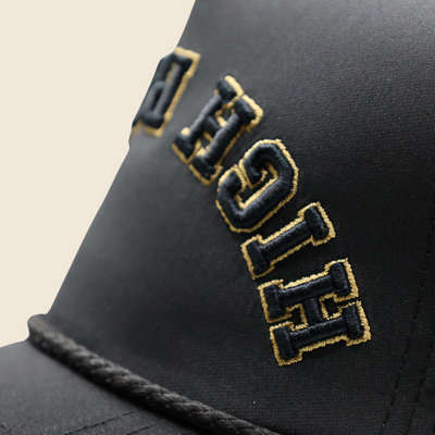 Close-up of gold High Roller embroidery and black rope trim on a black hat