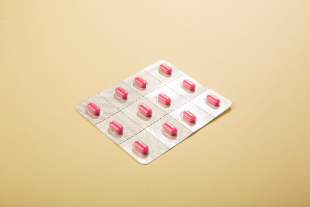 A photo of a pillpack showing pink pills laying on a yellowish colored table.